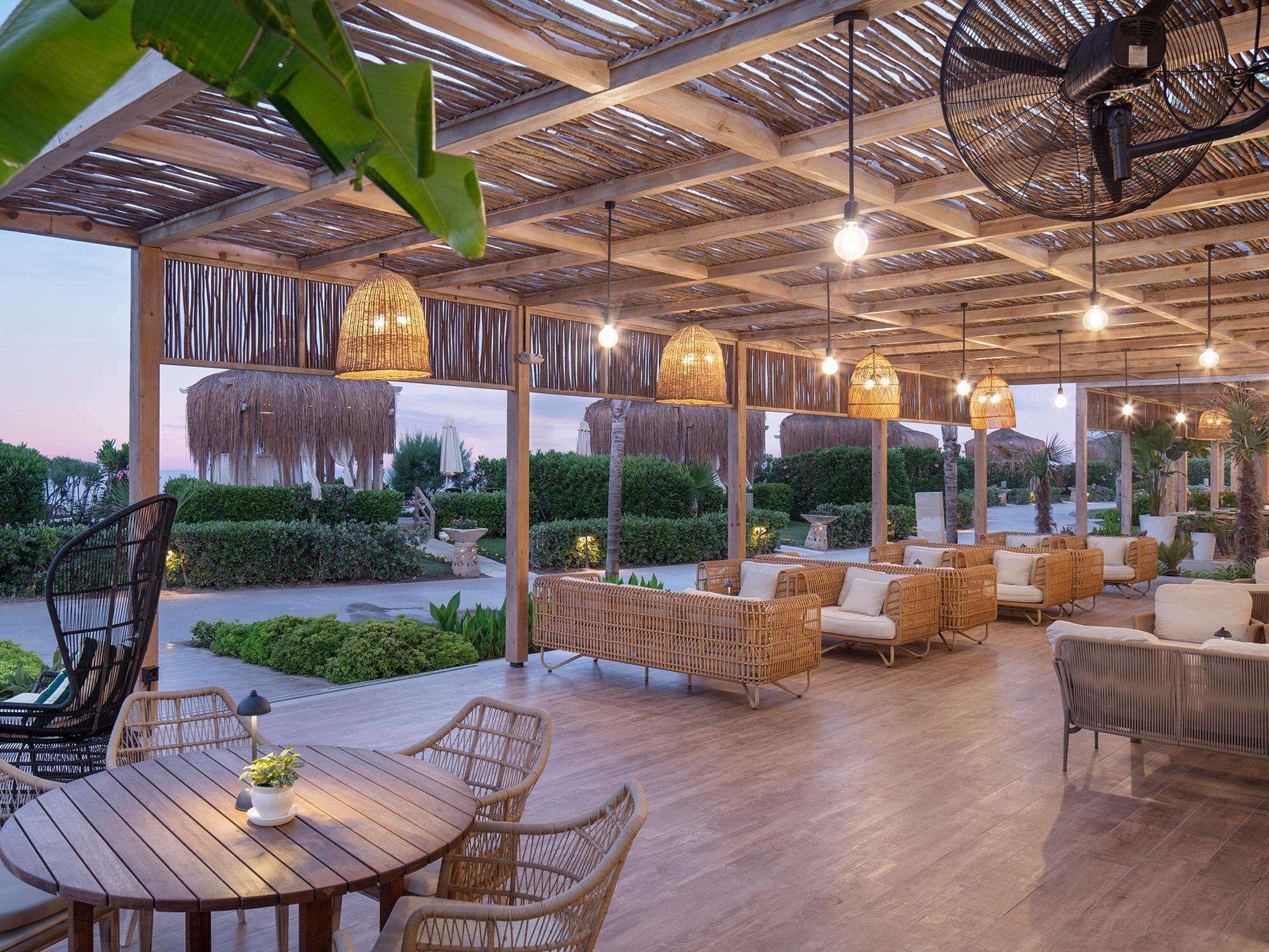 An outdoor seating area with wicker furniture and hanging lights, overlooking a landscaped garden.
