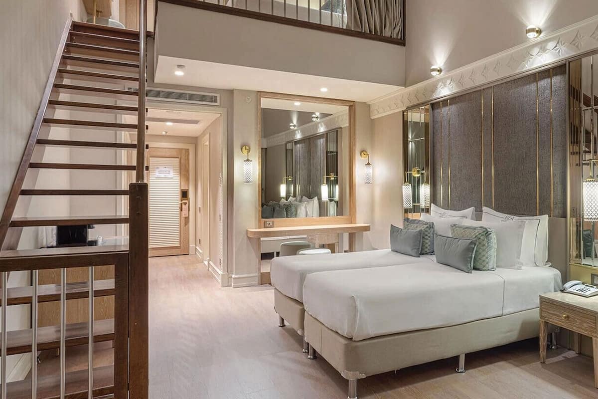 Ein Schlafzimmer mit einem großen Bett, einem Schreibtisch, einem Sessel, einer Couch, einem Spiegel und einer Treppe.