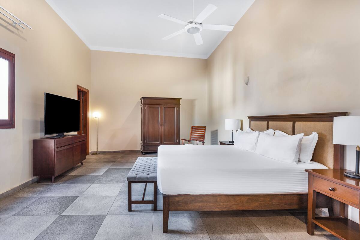 Habitació d'hotel amb un llit gran, una televisió, un armari de fusta, una cadira i un escriptori amb una làmpada.