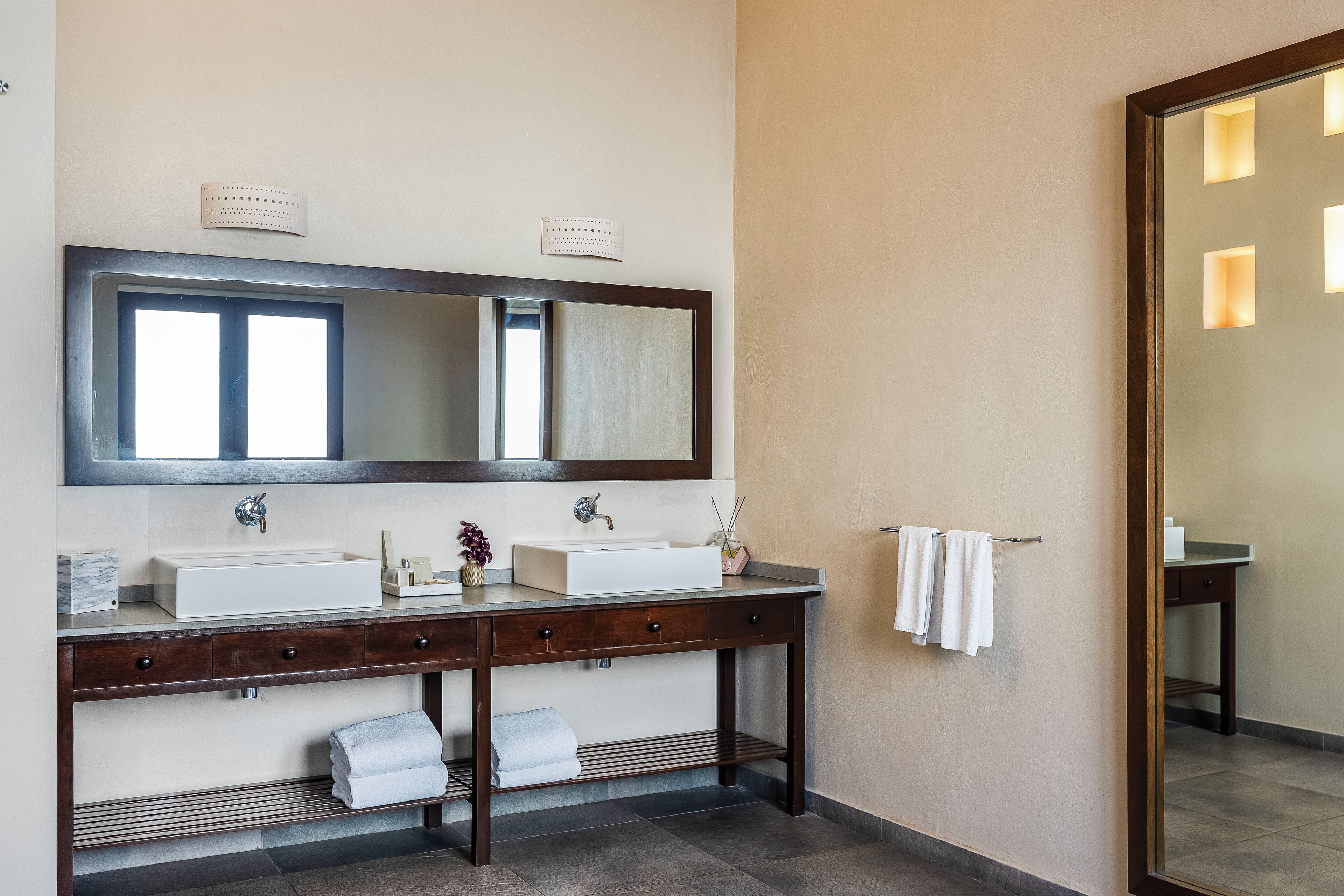 A bathroom with a large mirror, two sinks, and a towel rack.