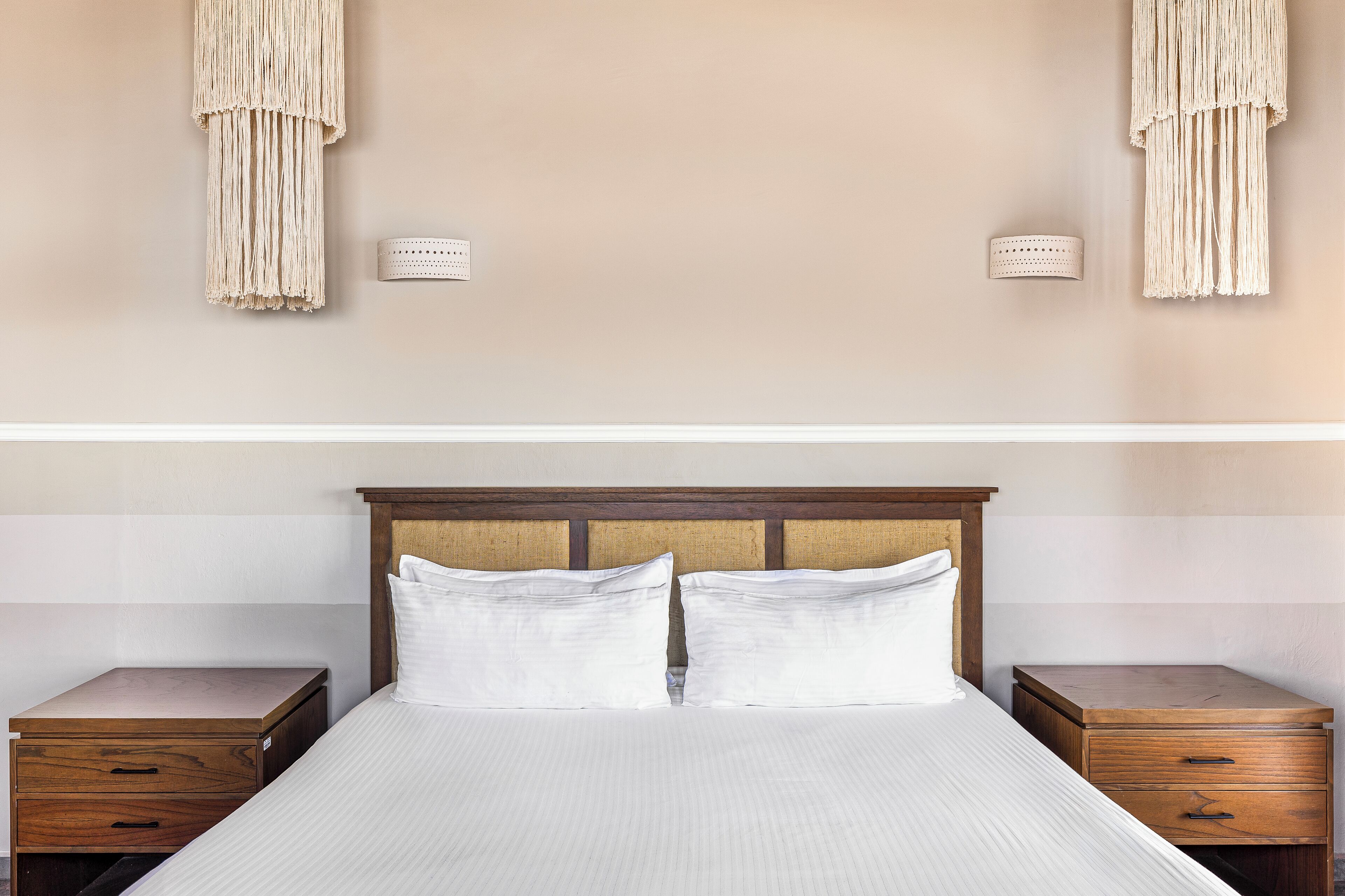 A neatly made bed with white linens, two wooden nightstands with drawers, and a wooden headboard.
