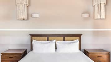 A neatly made bed with white linens, two wooden nightstands with drawers, and a wooden headboard.