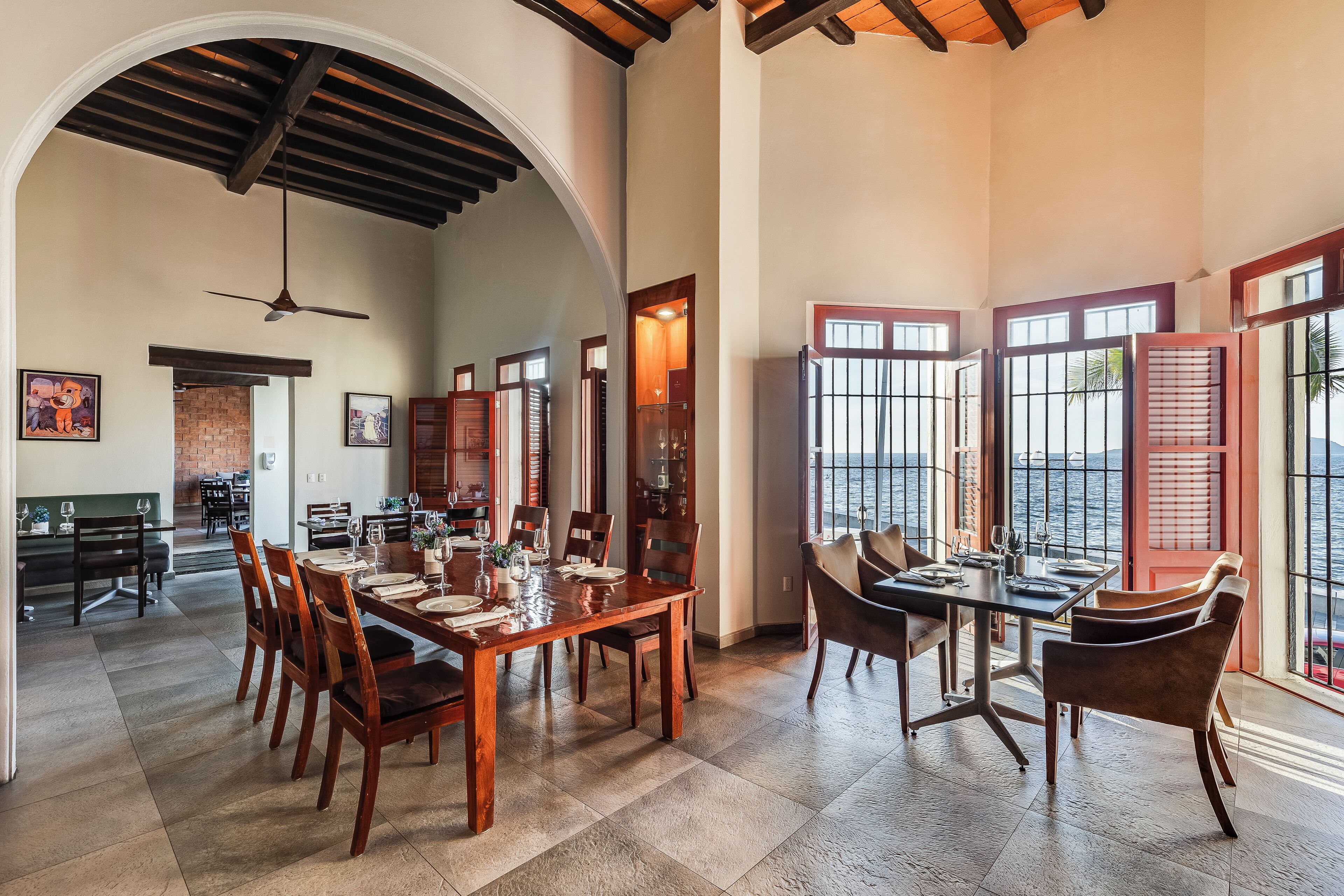 A spacious dining area with a high ceiling, large windows, and a view of the sea.