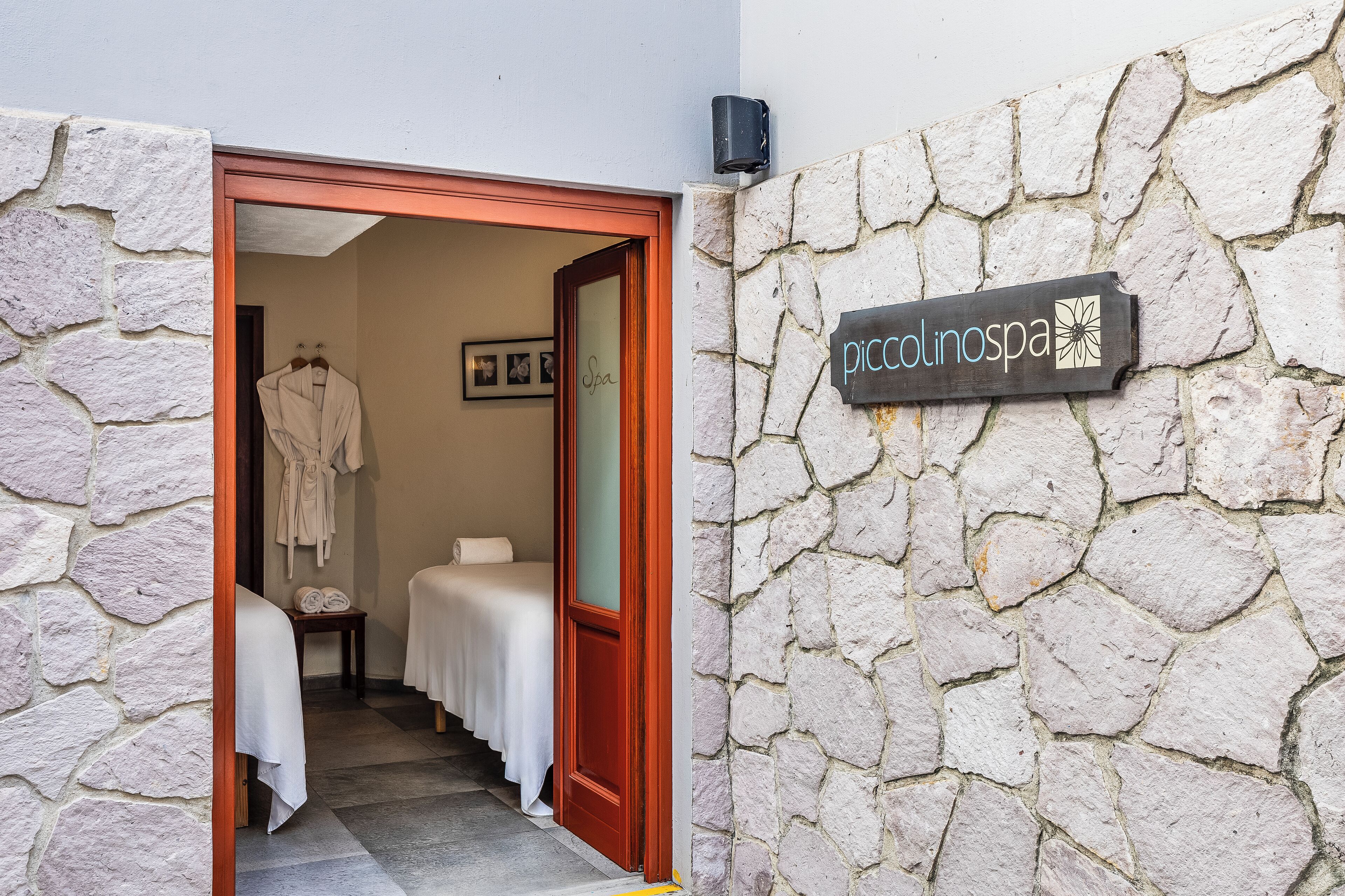 A spa entrance with a stone wall and a sign reading "piccolinospa".