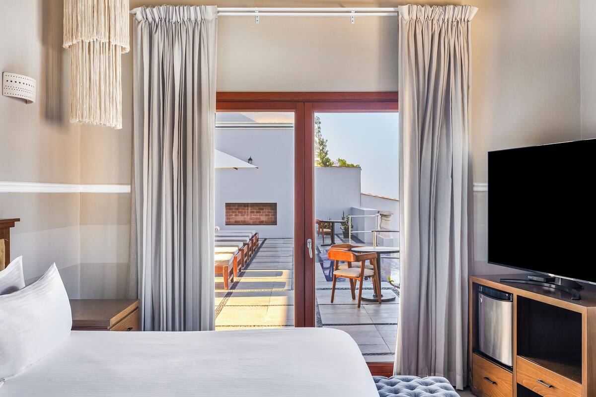 Habitació d'hotel amb un llit, televisió, armari de fusta i una porta corredissa de vidre que dona a una zona exterior amb seients.
