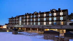 A multi-story hotel with a stone facade, multiple balconies, and a well-lit entrance area.