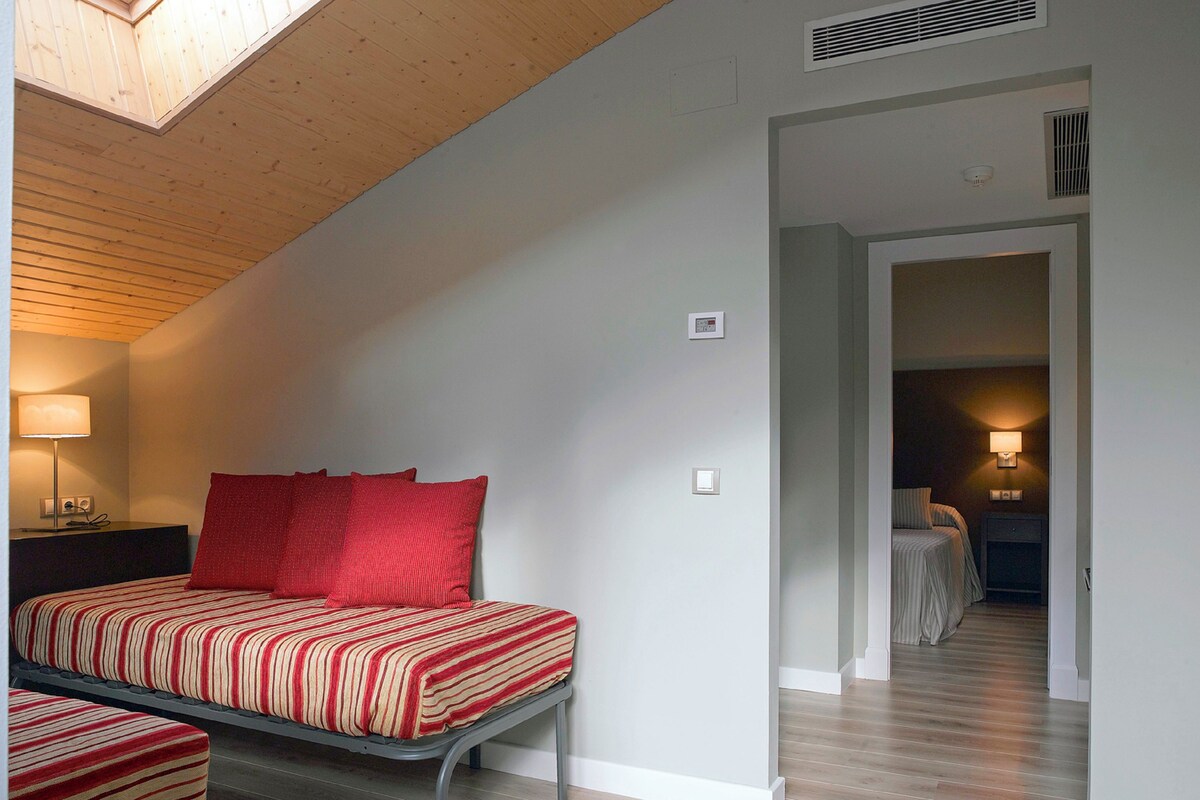 Un dormitorio con cama, mesita de noche, lámpara y techo de madera.