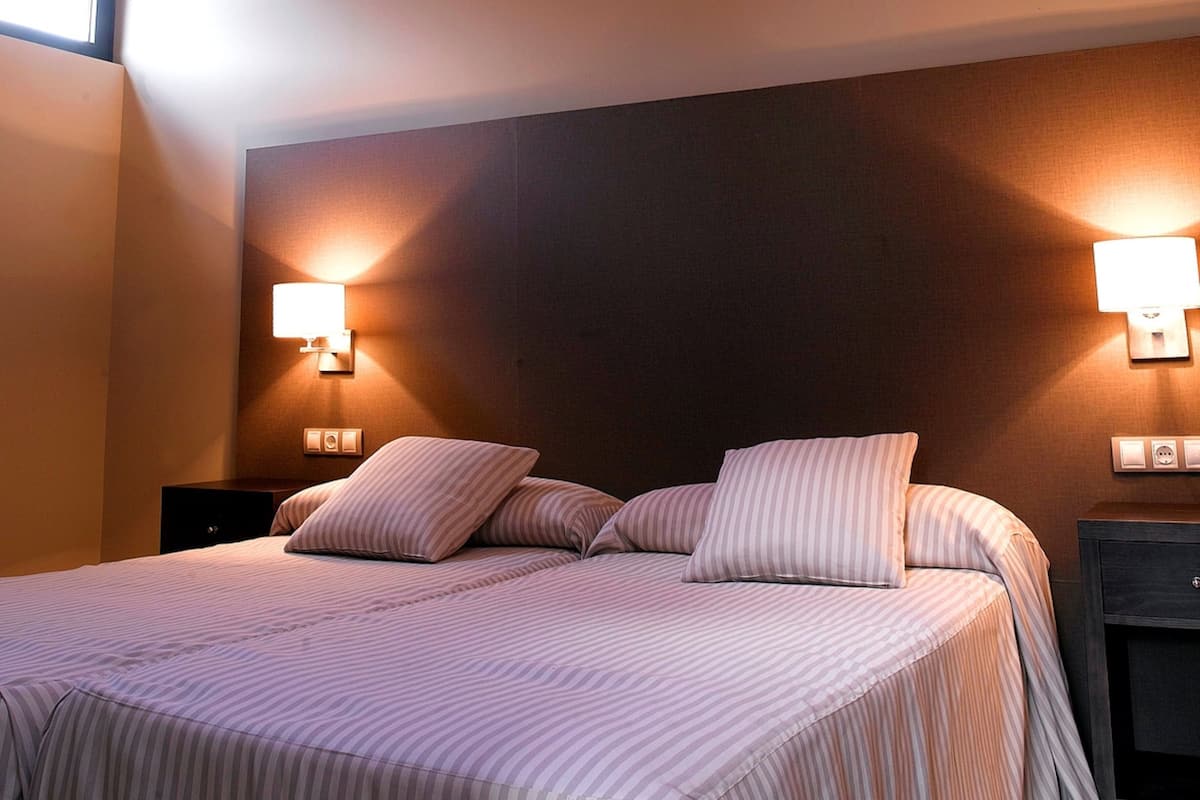 Una cama bien hecha con ropa de cama a rayas, dos lámparas de noche y un cabecero oscuro.