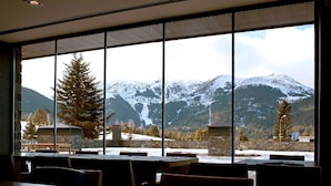 A restaurant with large windows offering a view of snow-covered mountains and trees.
