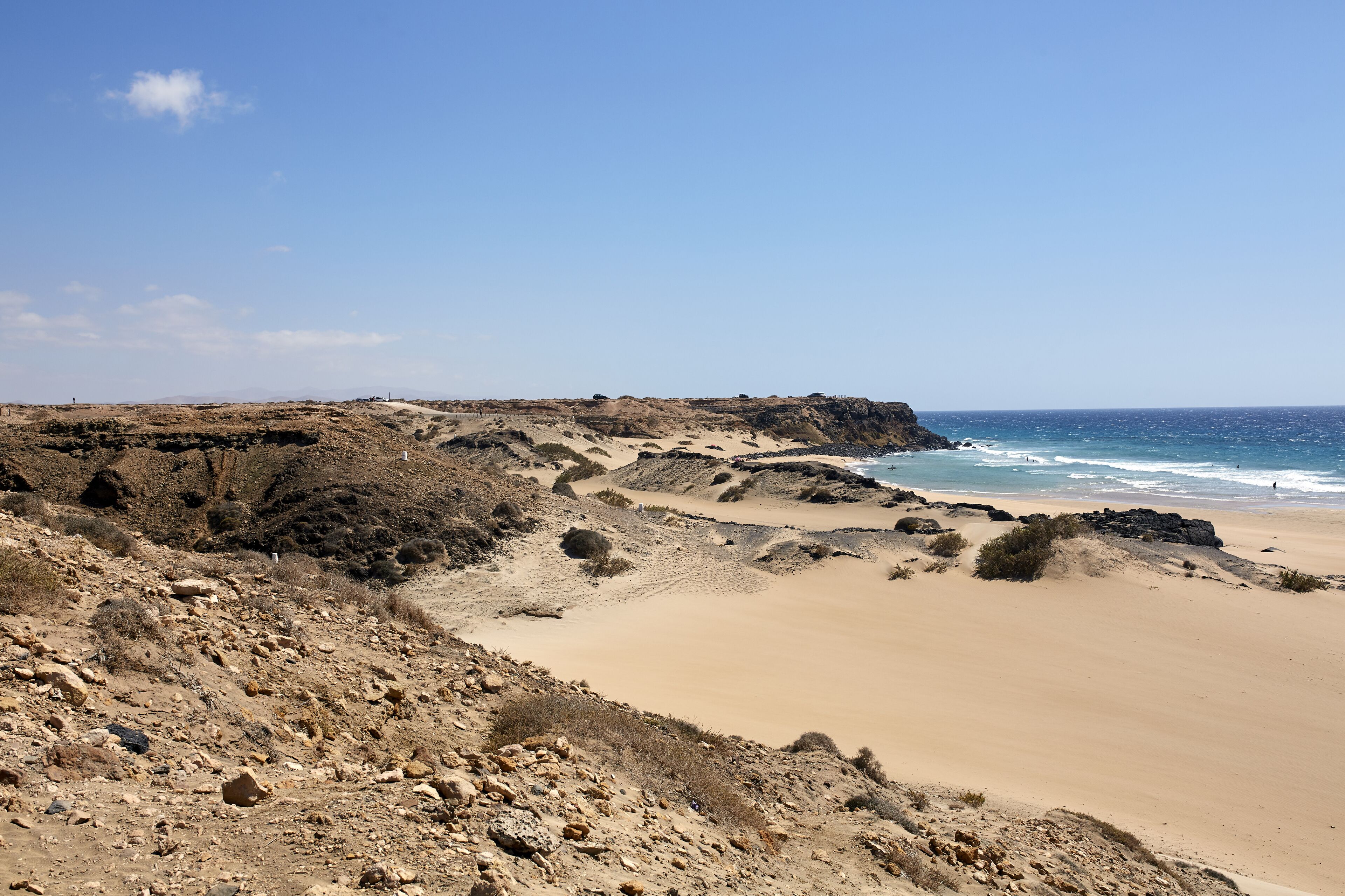 A coastal landscape with a sandy beach, rocky cliffs, and a clear blue sky.