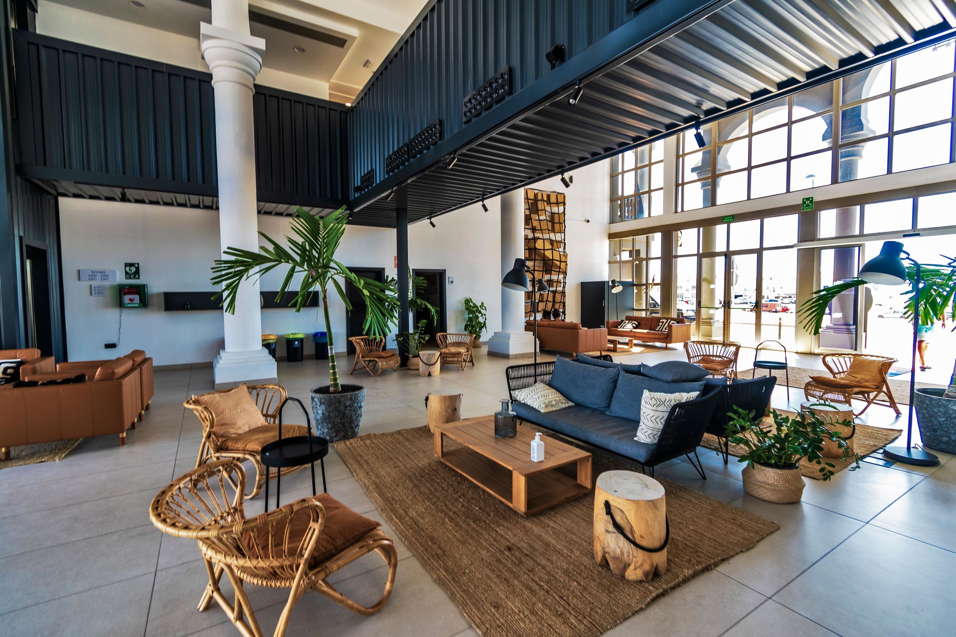 Eine großzügige Lobby mit hoher Decke, großen Fenstern und verschiedenen Sitzgelegenheiten, darunter Sofas, Sessel und ein Couchtisch.