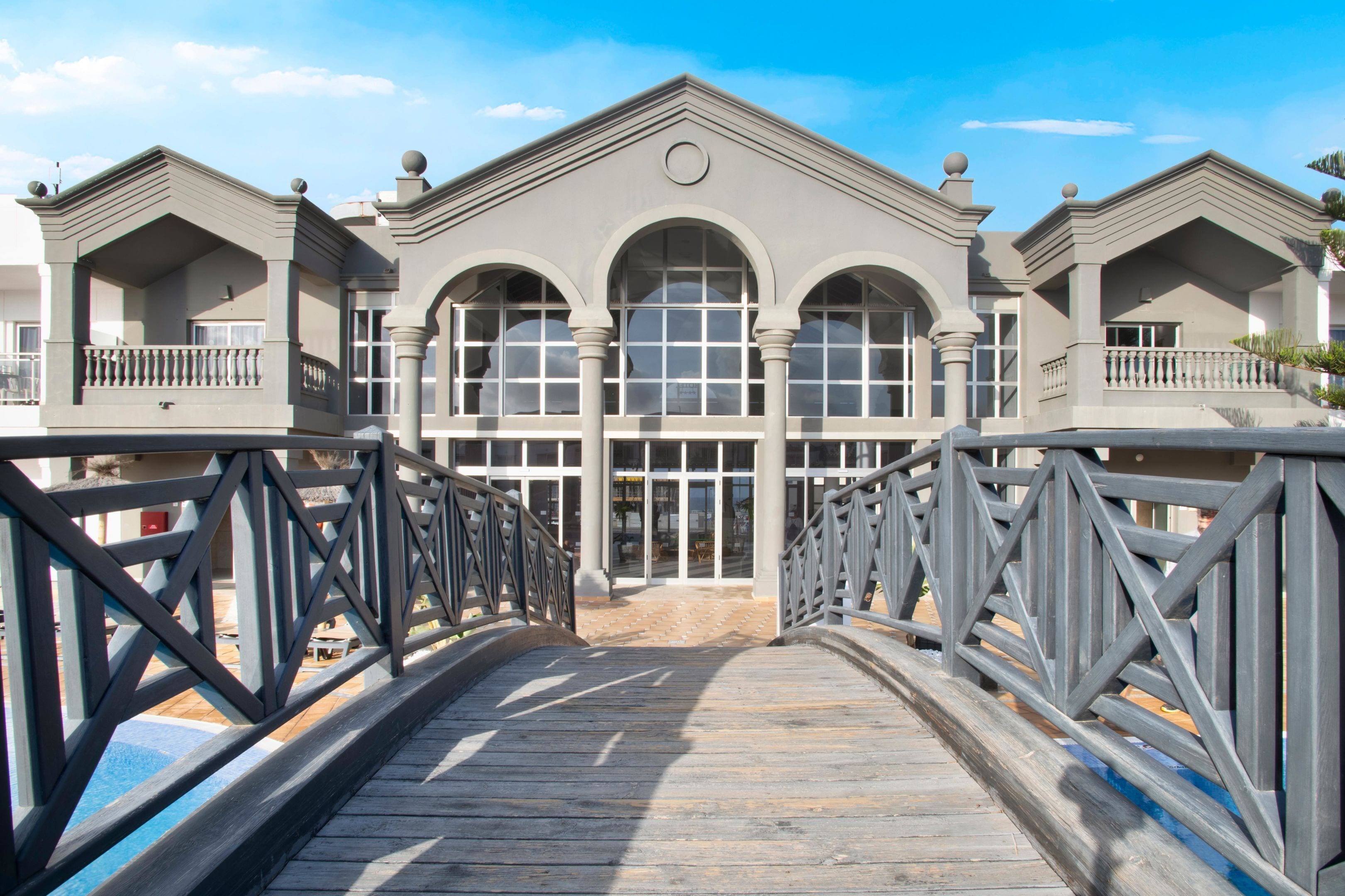 A hotel with a grand entrance, a wooden bridge, and a pool area.