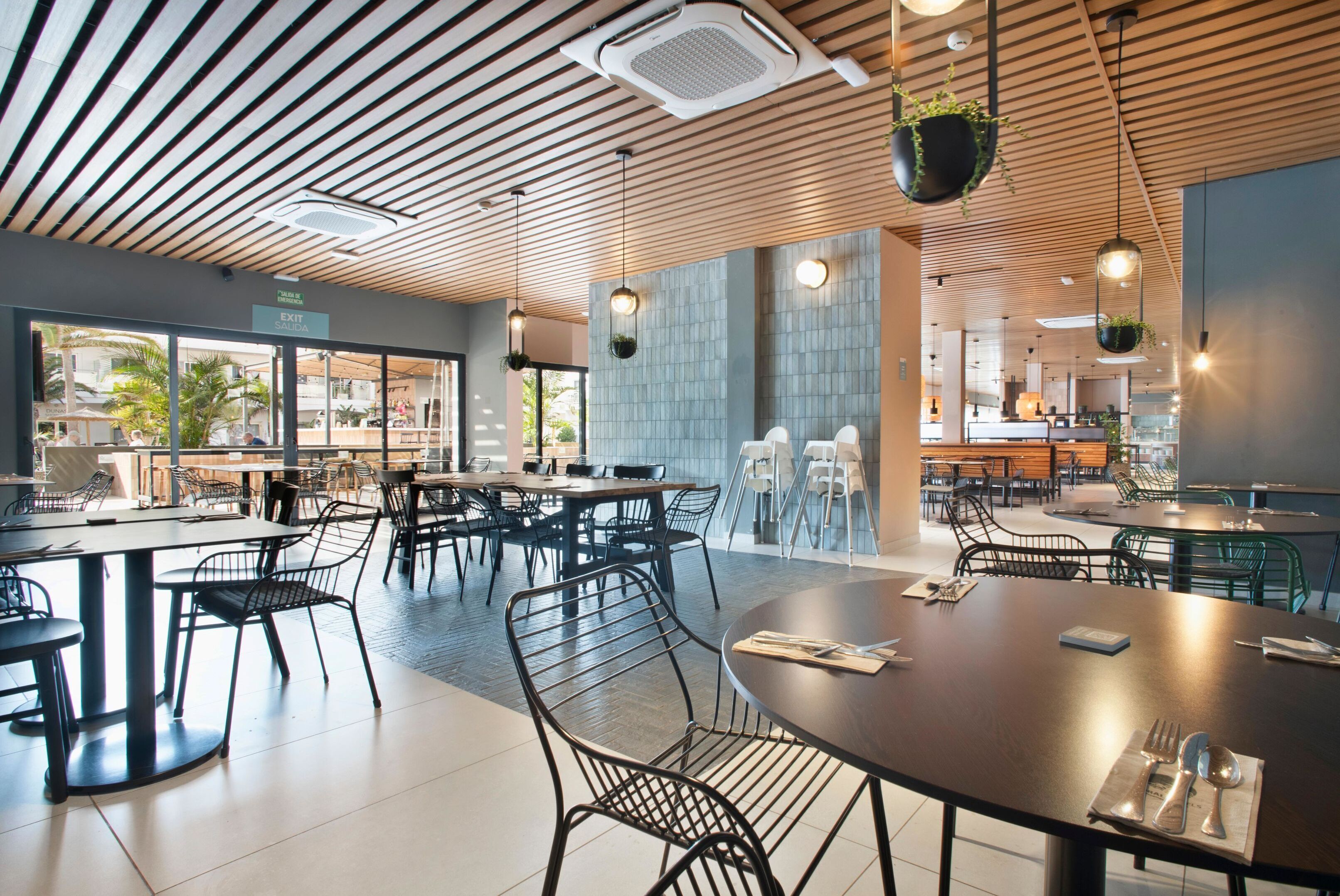 Un restaurant moderne avec un plafond en bois, des chaises en métal noir et des plantes suspendues.