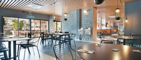 Un restaurant moderne avec un plafond en bois, des chaises en métal noir et des plantes suspendues.