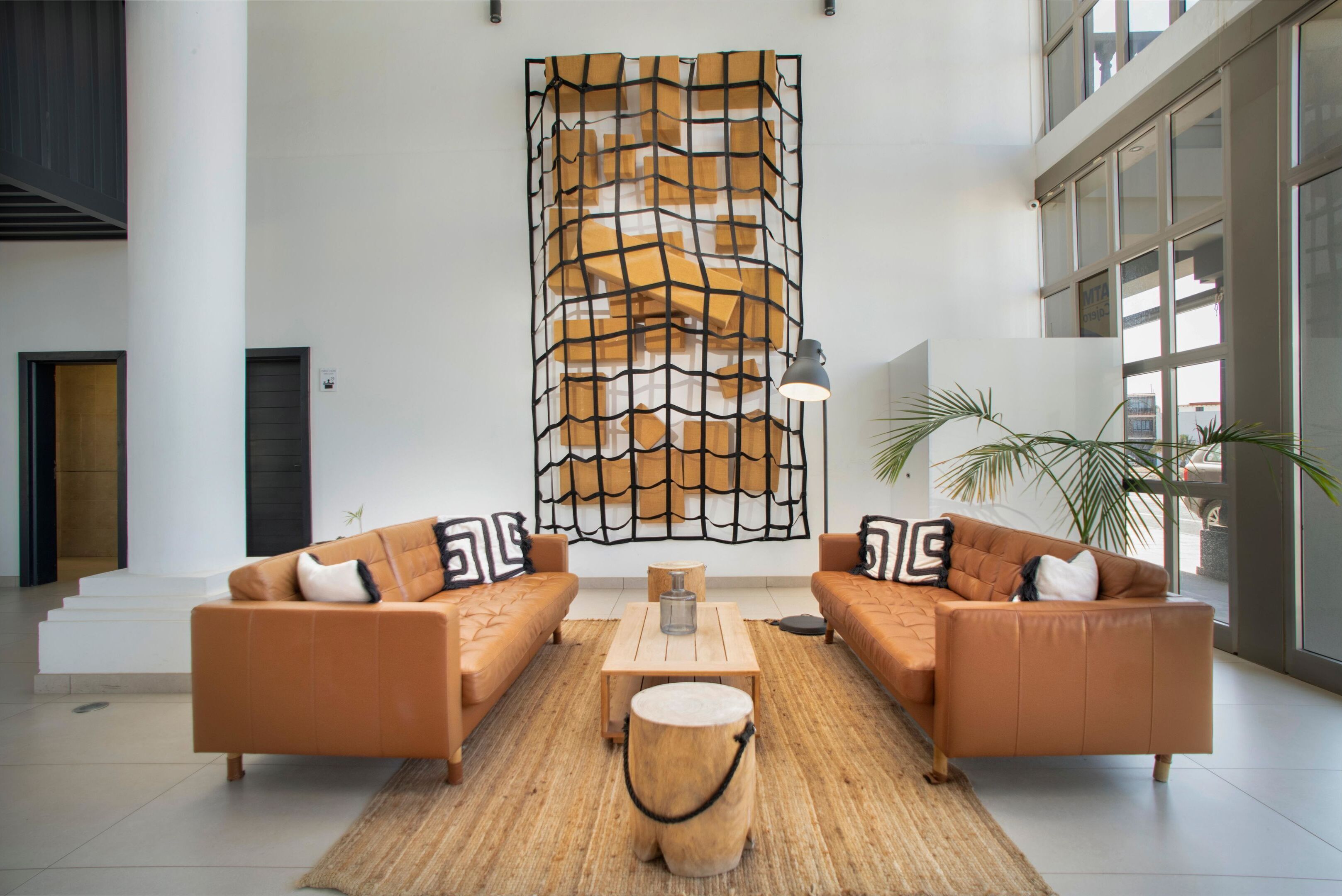 Um hall amplo com dois sofás de couro, uma mesa de centro, um tronco de madeira e uma grande obra de arte abstrata na parede.