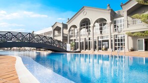 A swimming pool with a bridge, a building with arched windows, and a clear blue sky. - Coral Cotillo Beach (La Oliva)
