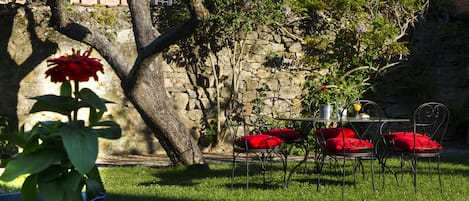 Eine Steinsäule, ein Metalltisch mit Stühlen und eine rote Blume im Vordergrund.