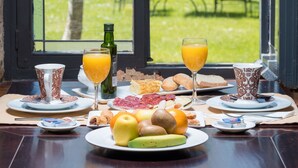 Une table de petit-déjeuner avec des assiettes remplies de nourriture, des verres de jus d’orange et une bouteille d’huile d’olive.