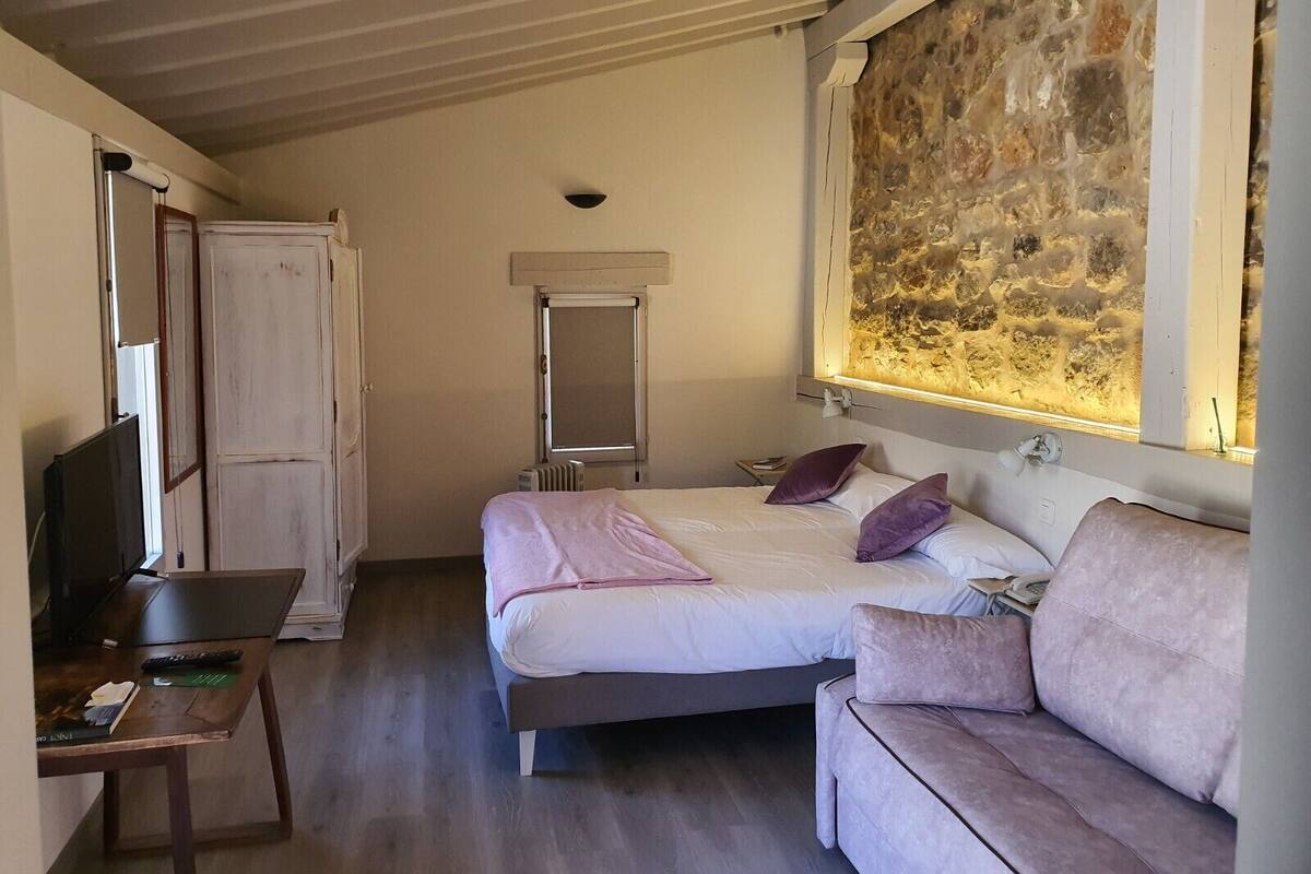 Een slaapkamer met een bed, een bank, een bureau en een stenen muur.