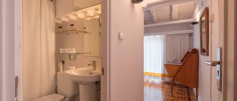 A bathroom with a toilet, sink, and shower. There is a mirror above the sink and a patterned floor. A staircase leads to another room.