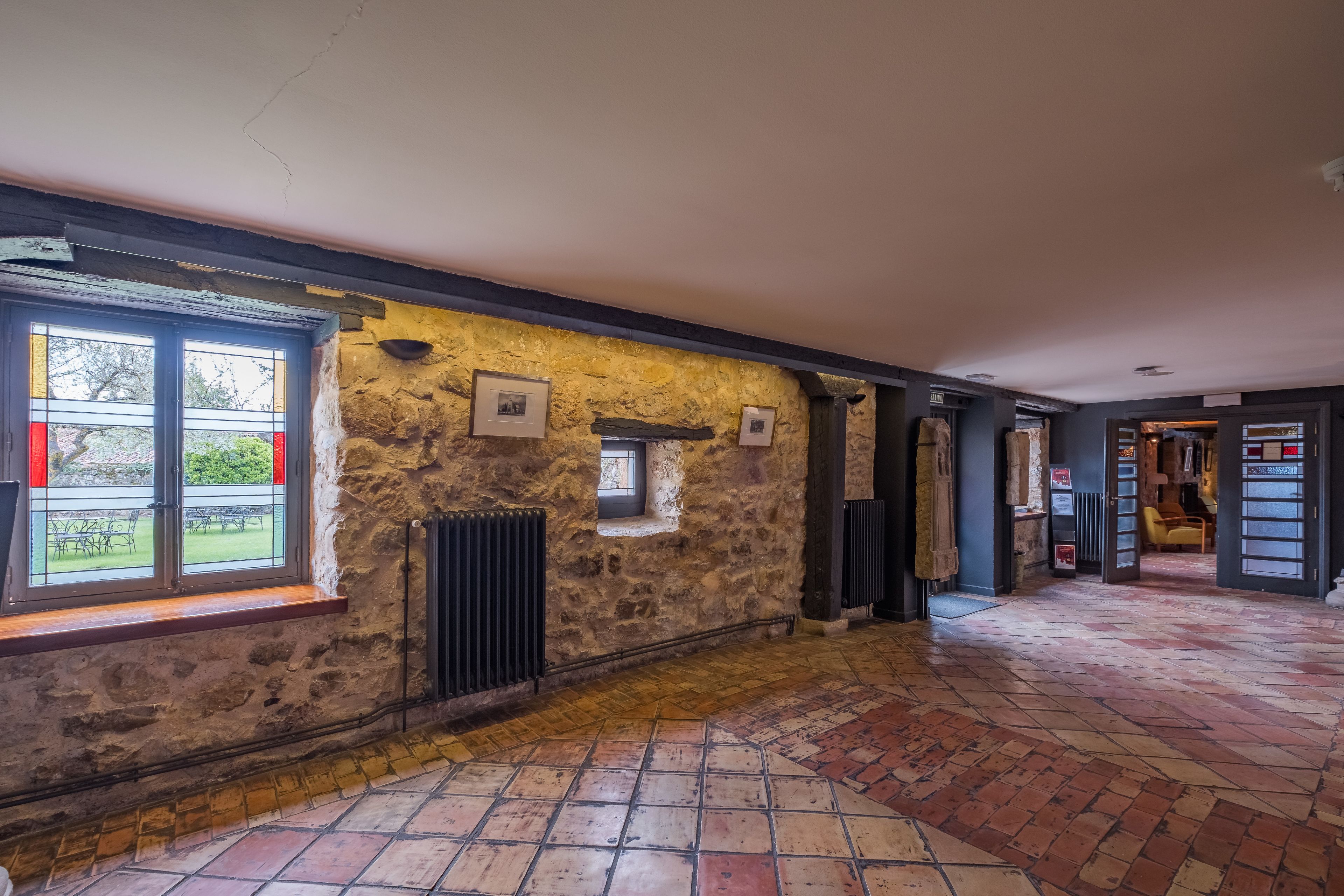 Una habitación con paredes de piedra, piso de baldosas y una ventana con cortinas rojas.