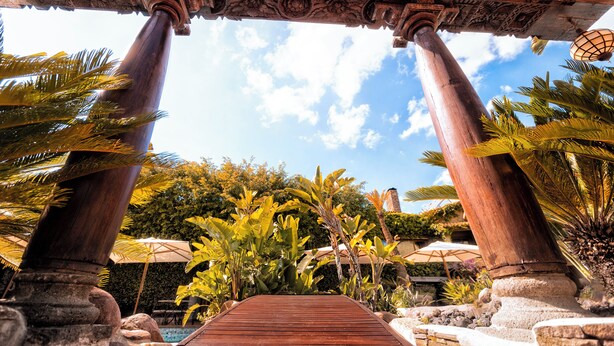 A pathway with ornate columns leading to a covered area, surrounded by tropical plants and umbrellas. - Hotel Swiss Moraira (Teulada)
