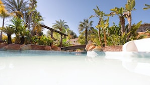 A swimming pool with a brick wall and palm trees in the background. - Hotel Swiss Moraira (Teulada)