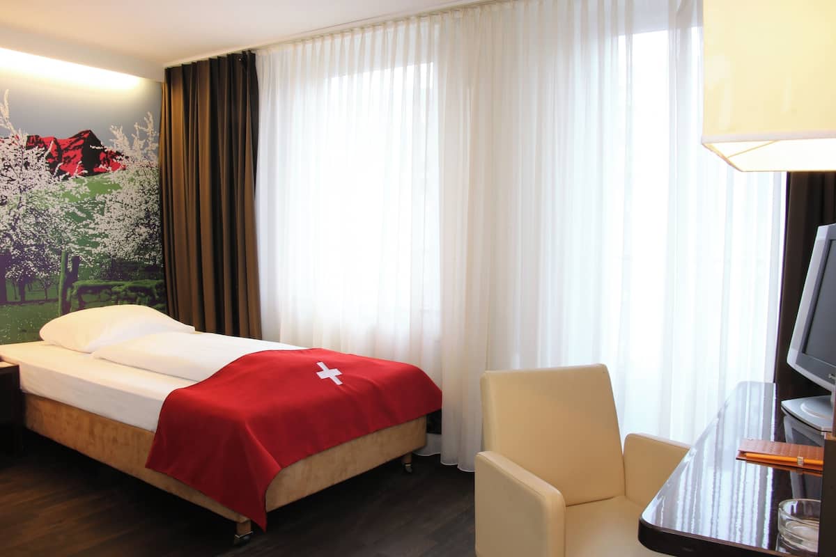 A hotel room with a bed, a chair, a TV, and a window with curtains.