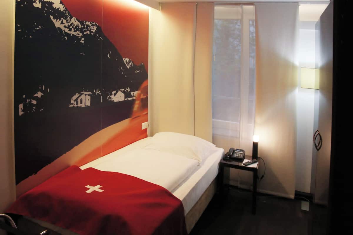 A hotel room with a bed, a nightstand with a phone, and a wall with a mountain landscape.