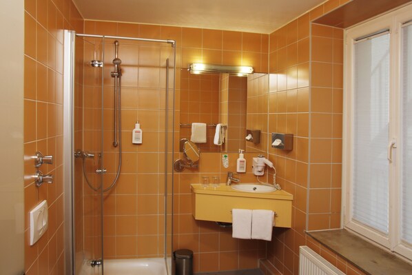 A bathroom with a glass-enclosed shower, a yellow sink, and a mirror above it.