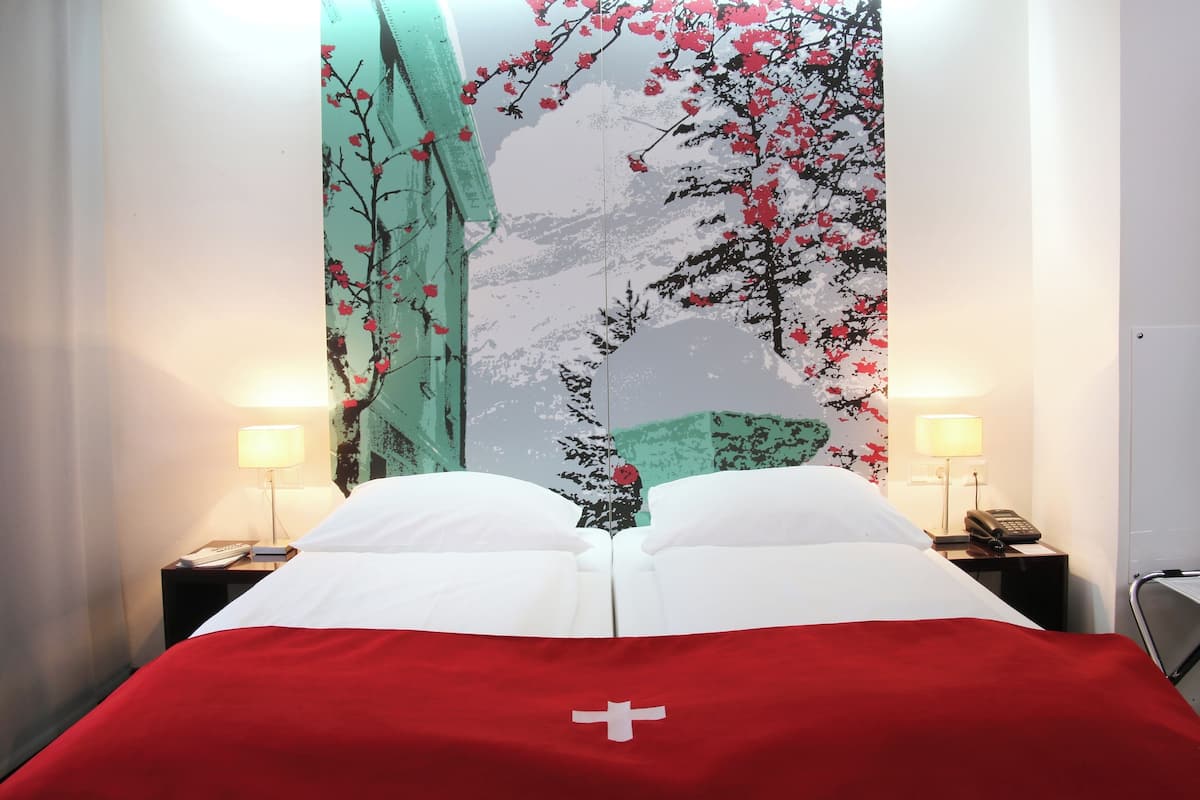 A hotel room with a bed, two bedside tables with lamps, and a large wall tapestry depicting a tree with red flowers.