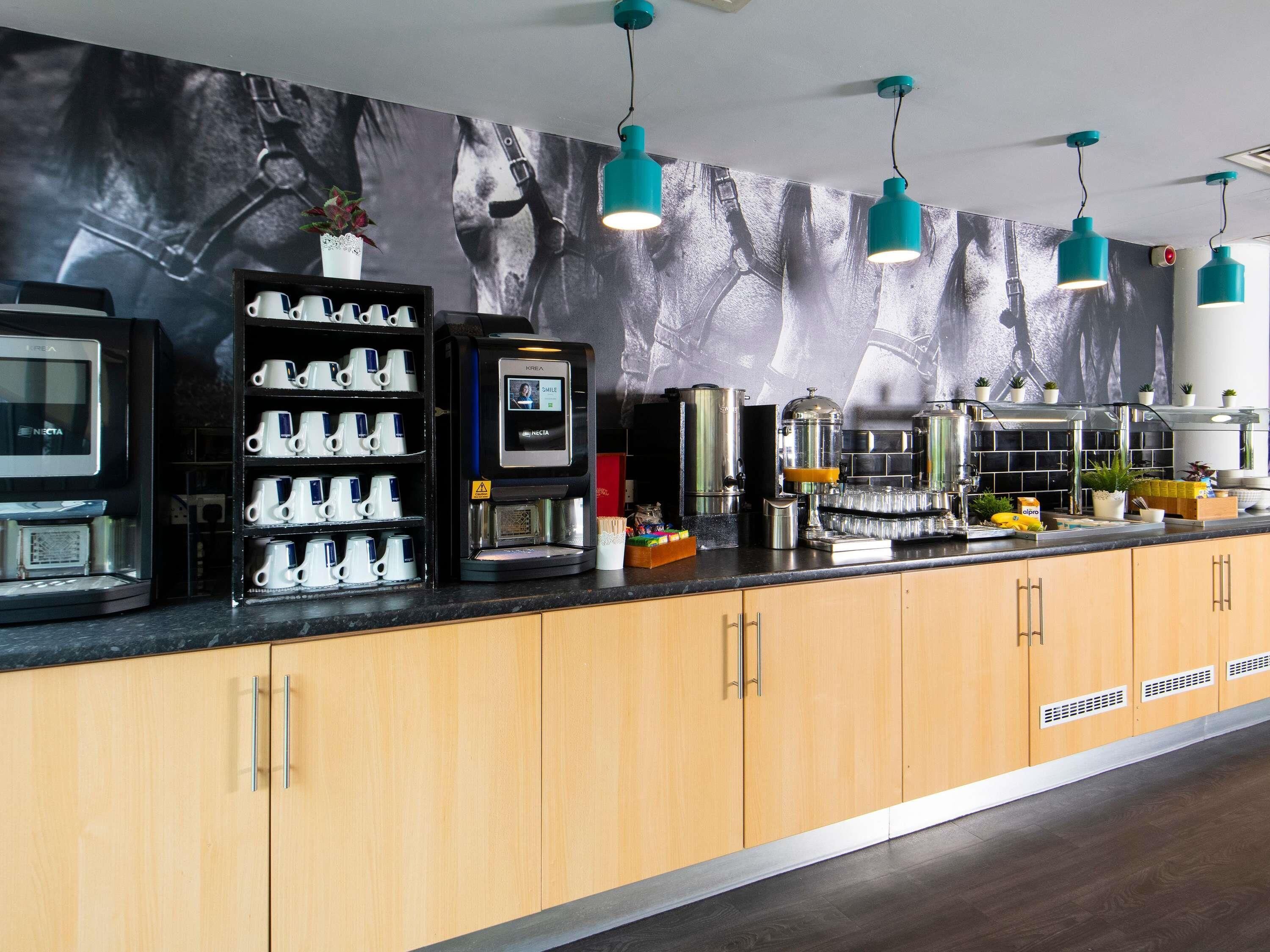 Una estación de café moderna con una máquina de café, varias tazas y un dispensador de café en la pared.