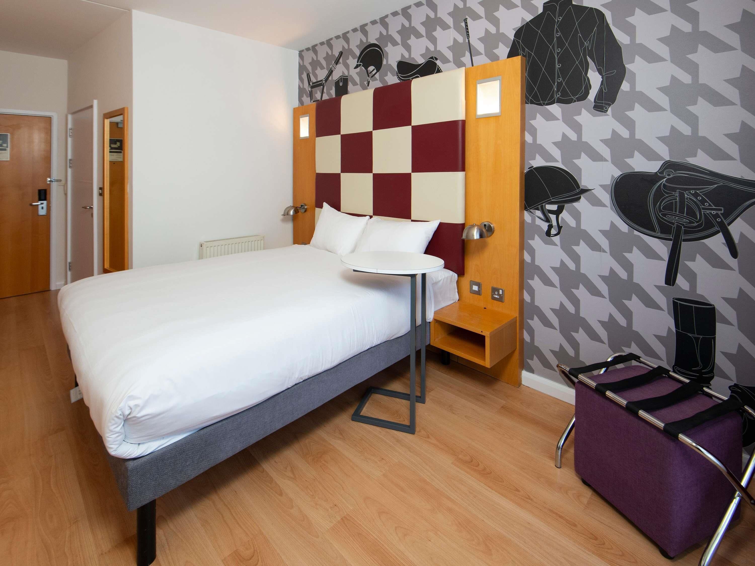 A hotel room with a bed, a small table, a chair, and a wall with a geometric pattern.
