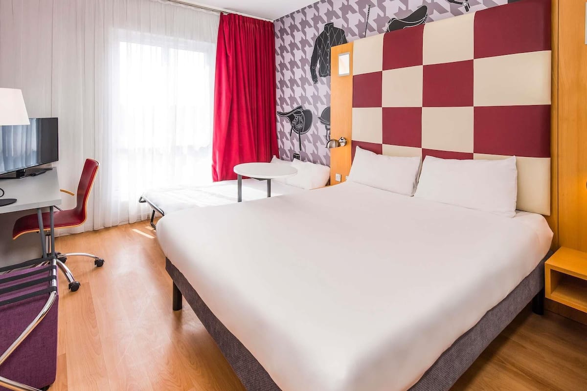Une chambre dâhĂŽtel avec un grand lit, un bureau avec une chaise, une petite table ronde et un tĂ©lĂ©viseur.