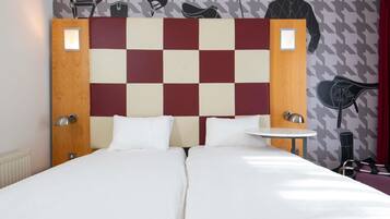 A double bed with a checkered headboard, two bedside tables, and a wall with sports-themed artwork.