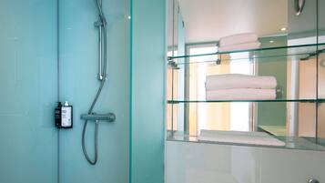 Un baño moderno con cabina de ducha de vidrio, repisa de vidrio con toallas dobladas y ducha de mano.
