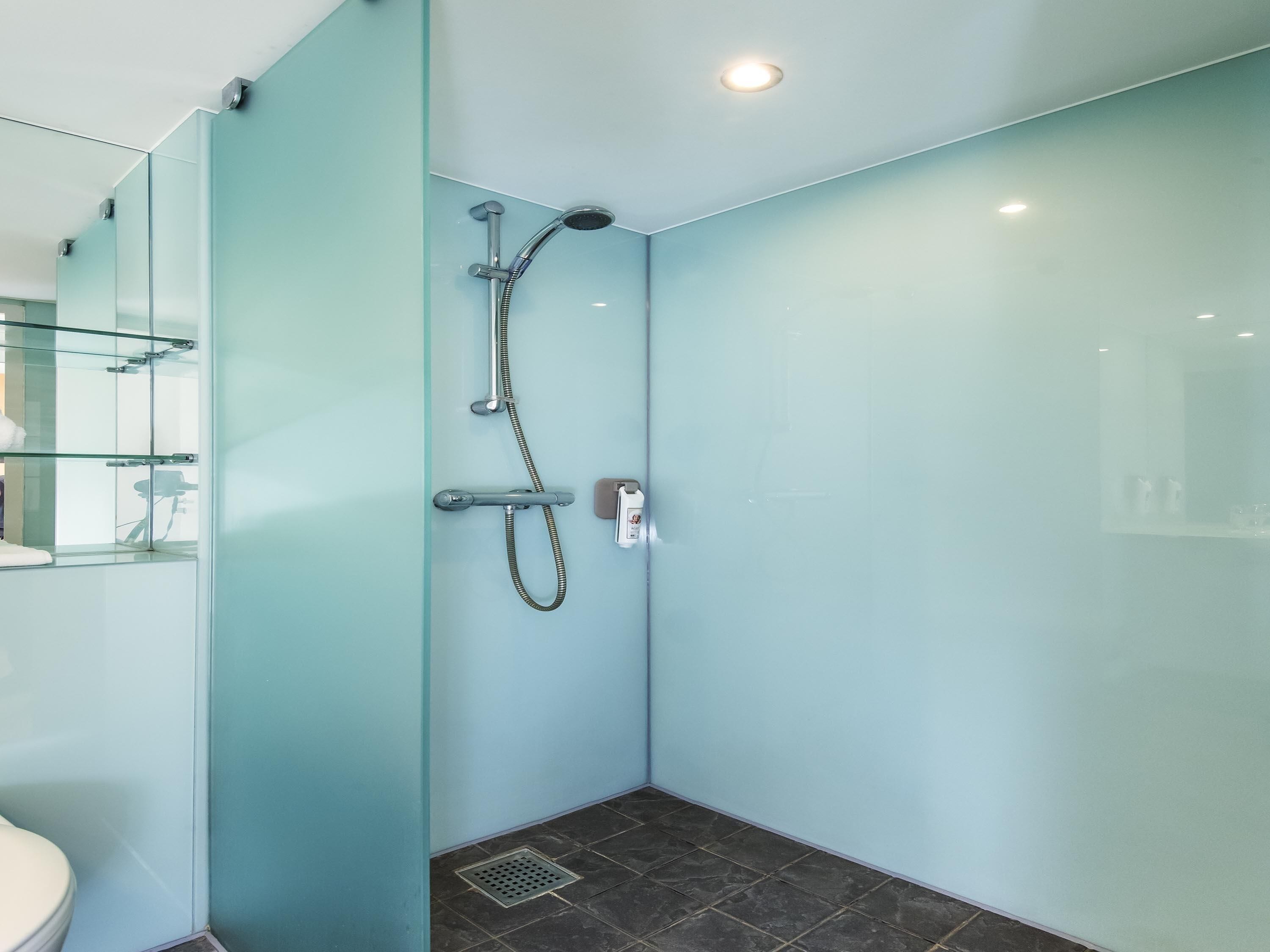 A modern bathroom with a glass shower enclosure, a toilet, and a glass shelf with toiletries.