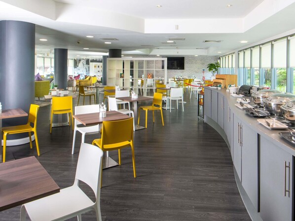 A modern dining area with a variety of seating options, including yellow and white chairs, and a buffet counter with food service equipment.