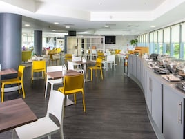 Un moderno comedor con diversas opciones de asientos, incluidas sillas amarillas y blancas, y un mostrador de buffet con equipo para servicio de alimentos.