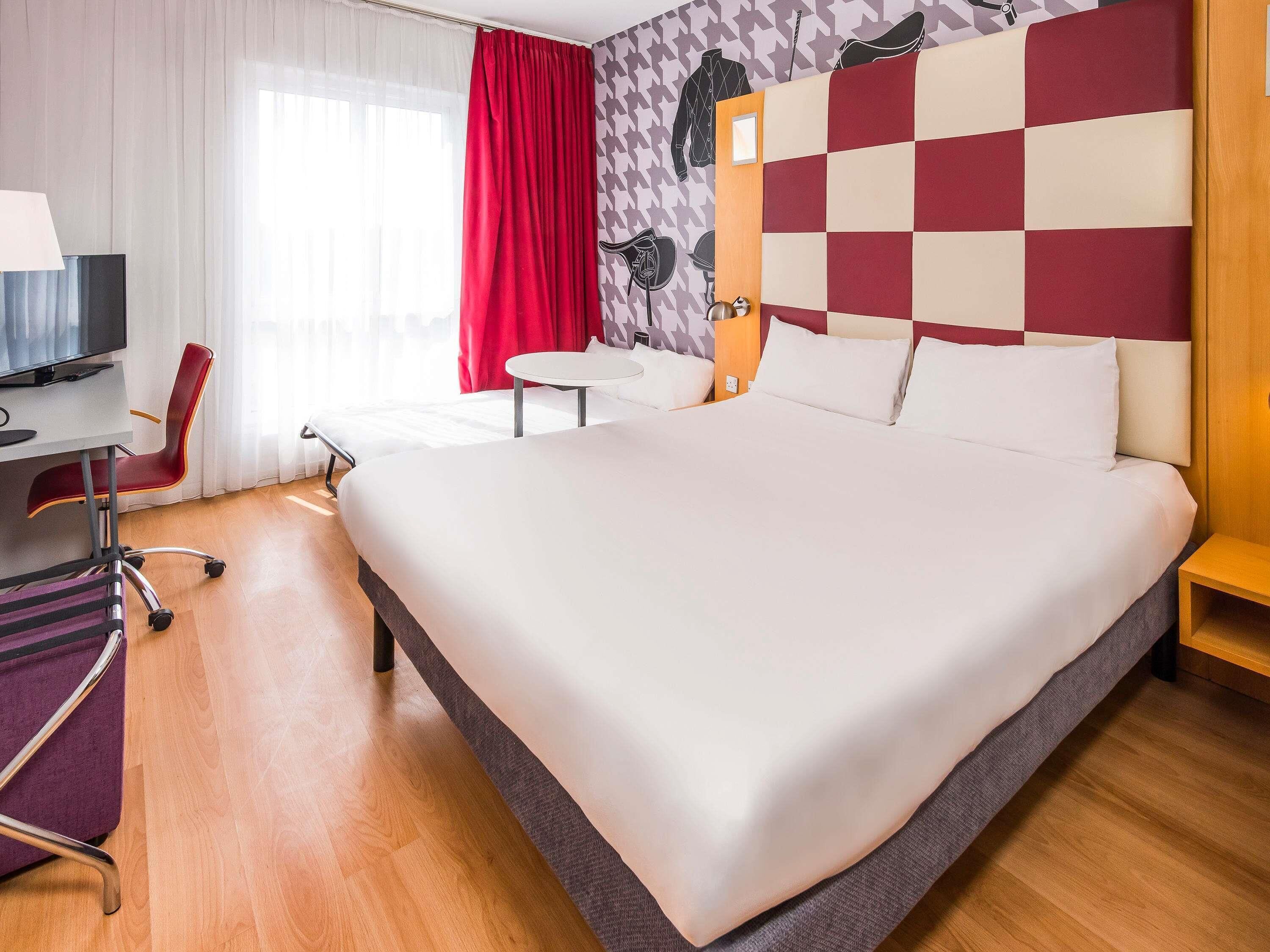 A hotel room with a large bed, a desk with a chair, a small table, and a TV.