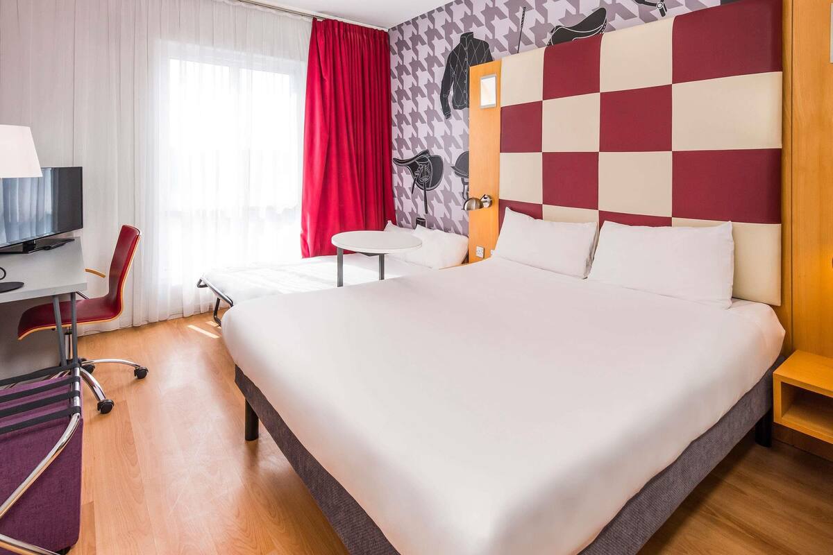 Habitación de hotel con una cama grande, un escritorio con silla, una mesita y un televisor.