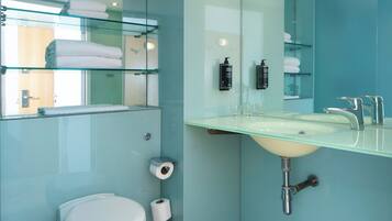 Un baño moderno con cabina de ducha de vidrio, inodoro blanco y lavamanos con espejo superior.