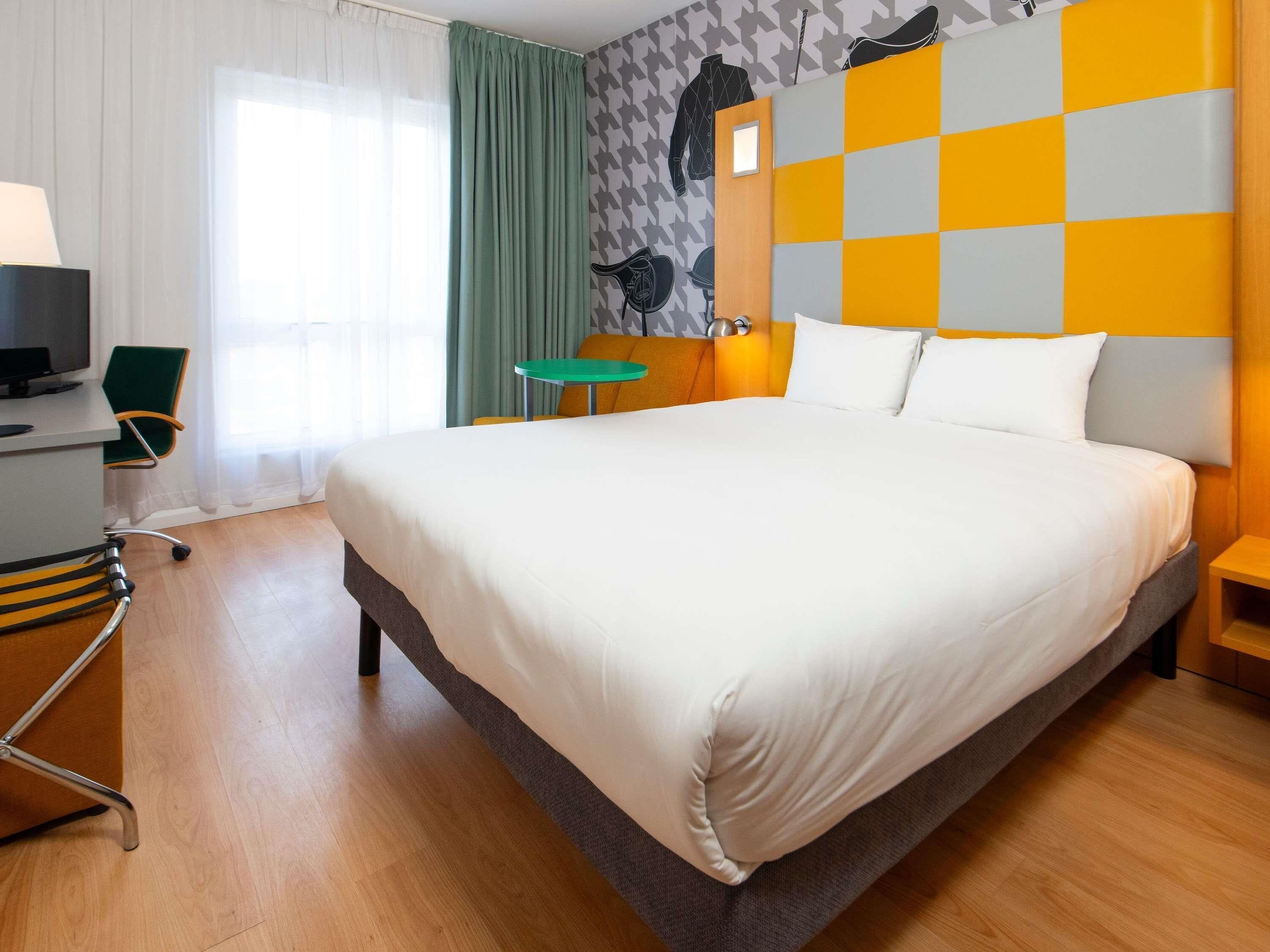 A hotel room with a large bed, a desk with a chair, a TV, and a window with curtains.