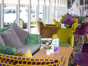 A modern interior with a sofa, chairs, a coffee table, and a view of the street through large windows. - Ibis Styles Haydock (St Helens)