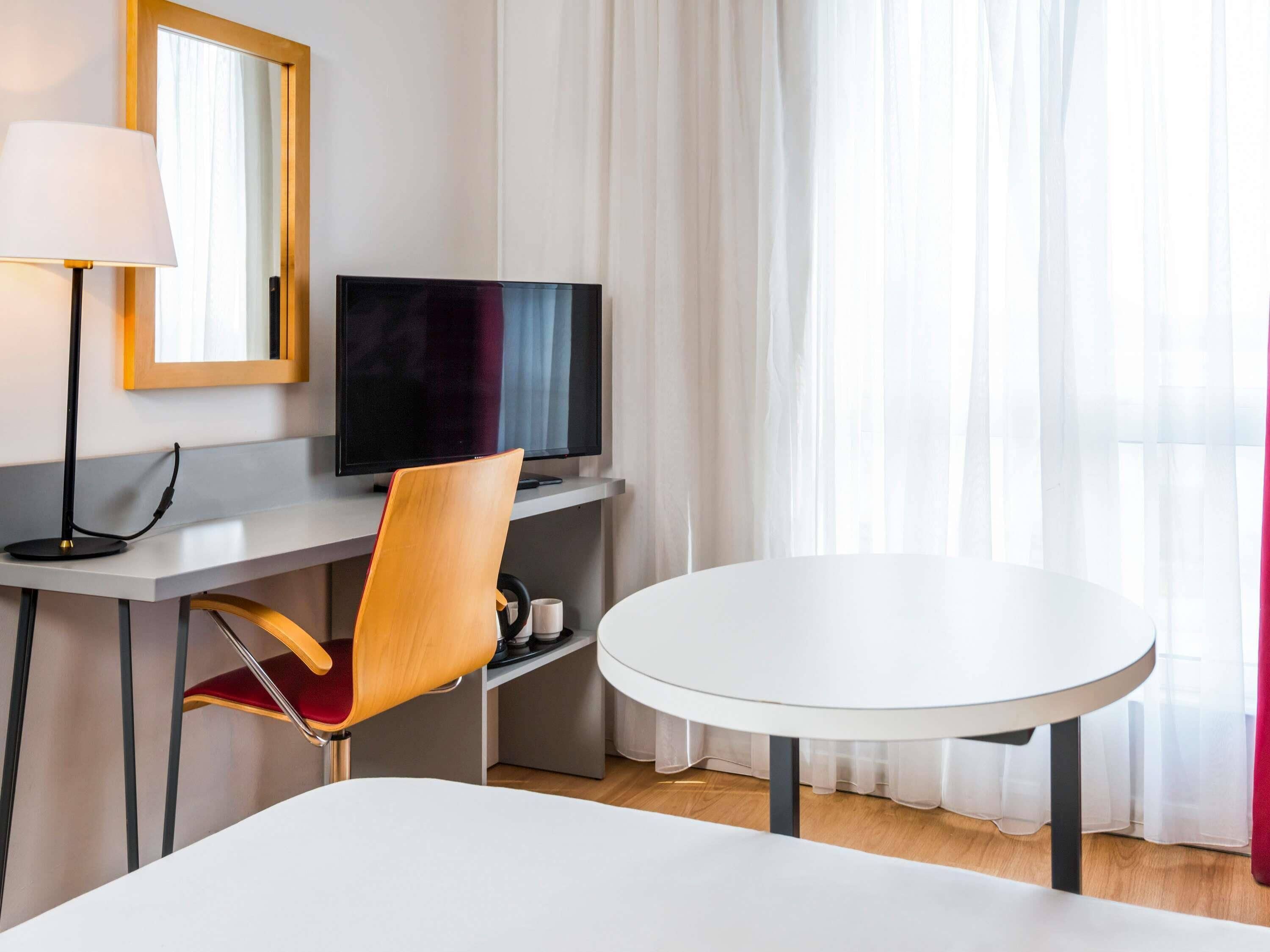 Une chambre d’hôtel comprenant un lit, un bureau avec une télévision, une chaise et une table ronde.