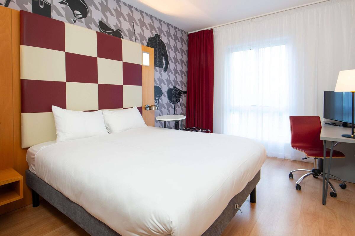 Una habitación de hotel con una cama grande, un escritorio con una silla, una mesita y un televisor.