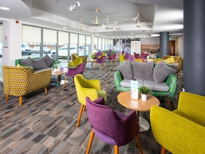 A hotel lobby with colorful seating, large windows, and a patterned carpet. - Ibis Styles Haydock (St Helens)