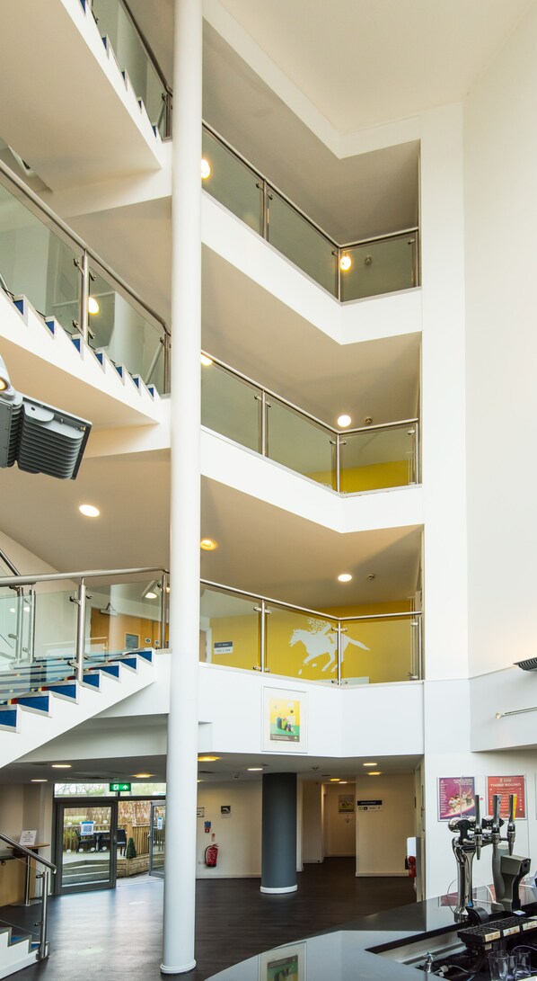 A multi-level atrium with glass railings, a central column, and a staircase. - Ibis Styles Haydock (St Helens)