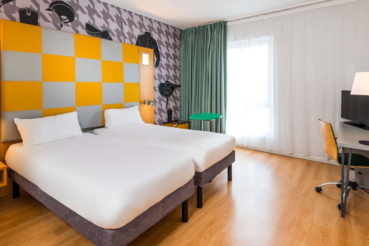 Habitación de hotel con cama doble, escritorio con silla, una mesita y televisión.
