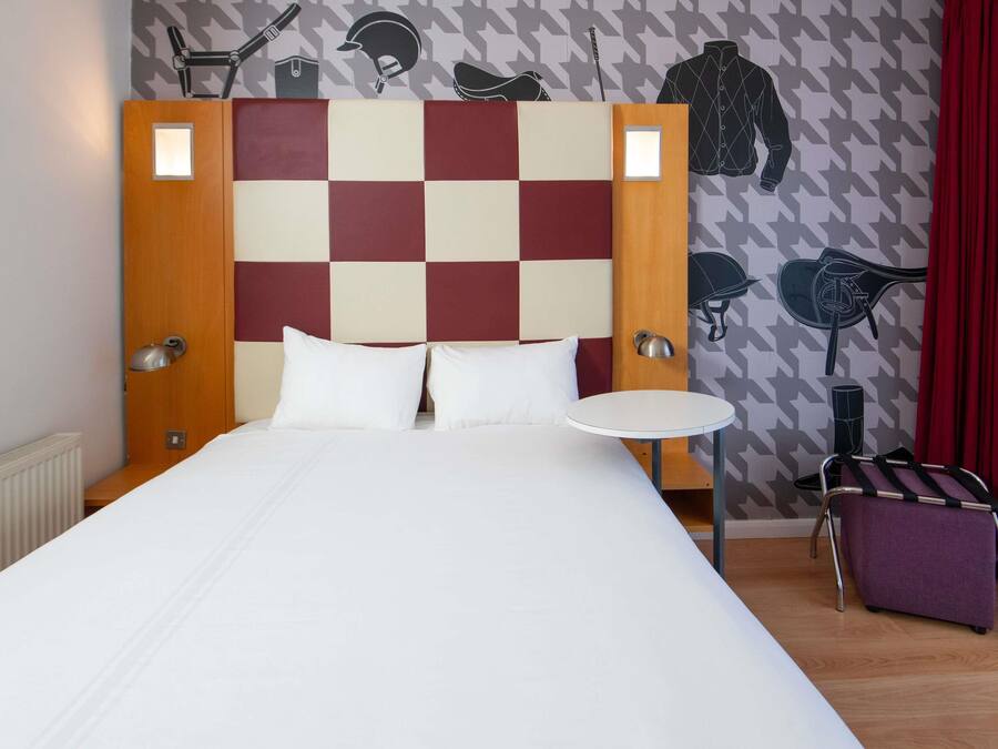 Habitació d'hotel amb capçalera de quadres, una taula rodona i un llit amb roba de llit blanca.